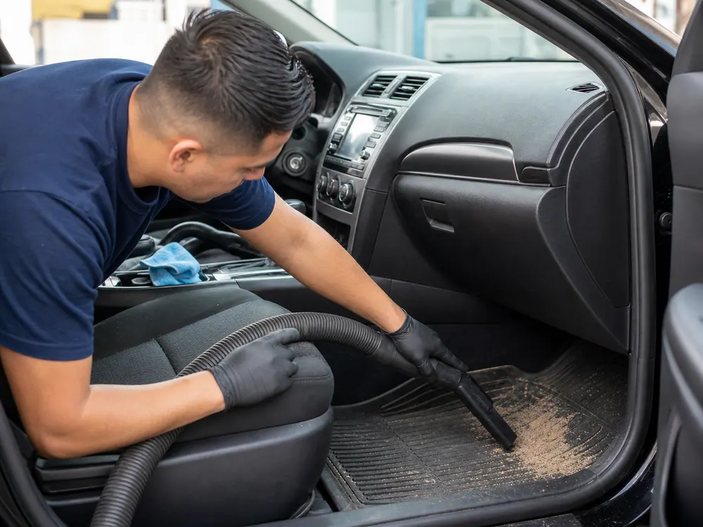 Worker vacuuming sandy mats and cargo area after a South Bay beach trip.